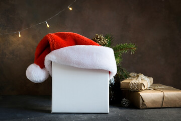 Mockup poster, Christmas canvas. Blank canvas frame with Santa hat and gift boxes on table. Festive...