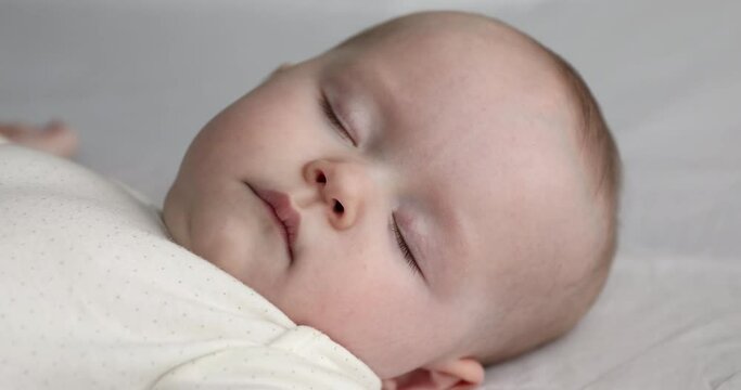 Sweet dreams. Close up of happy serene little 6 month baby child face sleeping tight on bed at home feeling satisfied calm relaxed. Cute carefree small infant kid dreaming napping with closed eyes