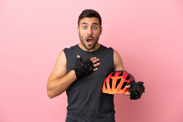 Young cyclist man isolated on pink background surprised and shocked while looking right - obrazy, fototapety, plakaty