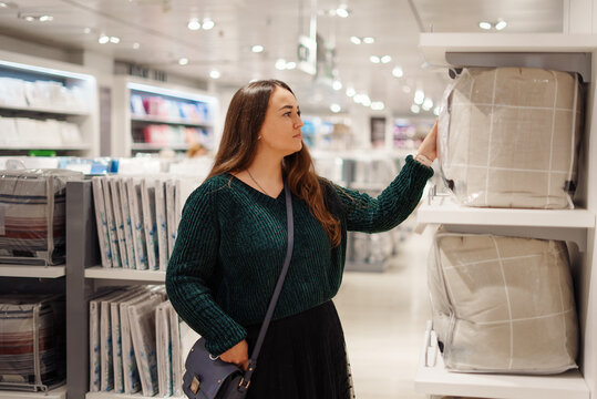 Young focused woman doing shopping in store mall in bedding department