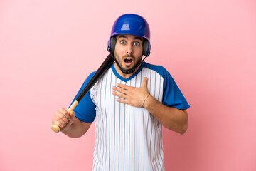 Baseball player with helmet and bat isolated on pink background surprised and shocked while looking...