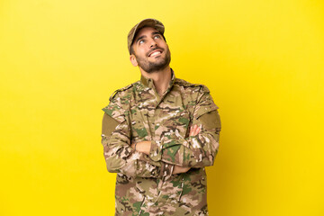 Military man isolated on yellow background looking up while smiling