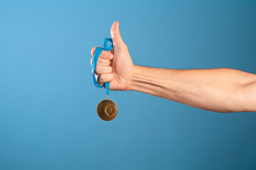 Win ,be a champion. Striving for achievements, concept, a man's hand squeezes the winner's gold medal, blue background