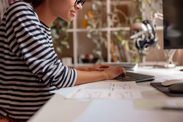 Close up of multiethnic lady sitting at the table with papers and typing on computer keyboard