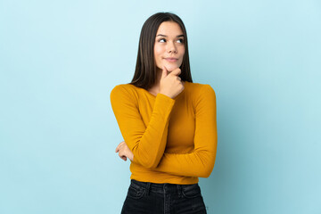 Teenager girl isolated on blue background thinking an idea while looking up