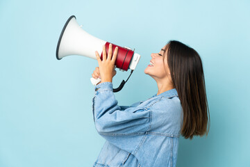 Teenager girl isolated on yellow background shouting through a megaphone to announce something in lateral position