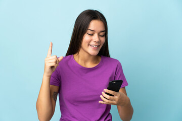 Teenager girl isolated on pink background using mobile phone and lifting finger