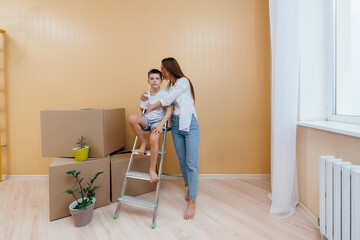 A young woman and her son are standing in front of the boxes and enjoying the housewarming after moving in. Housewarming, delivery and freight transportation, purchase of real estate.