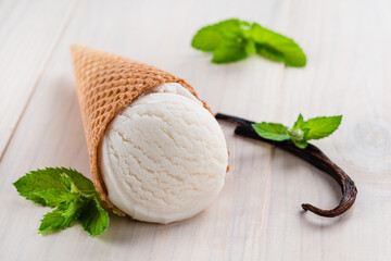 white ice cream with vanilla pod and mint in a cone on a white background