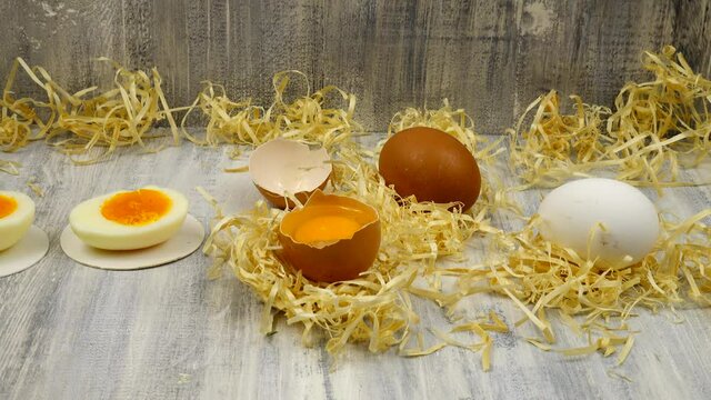 Chicken eggs, white and brown, raw and boiled, whole and cut in two, in eggshell and peeled, lie on a wooden table.