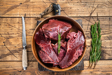 Sliced Beef or veal raw heart in a wooden plate with herbs. wooden background. Top View - obrazy, fototapety, plakaty