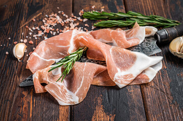 Dry cured Prosciutto crudo parma ham on a butcher knife. Dark wooden background. Top View