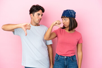 Young couple isolated on pink background showing thumb down sign with negative expression