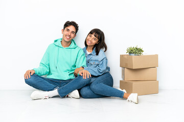 Fototapeta na wymiar Young couple making a move while picking up a box full of things sitting on the floor isolated on white background keeping the arms crossed in lateral position while smiling