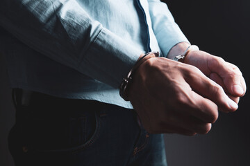 a young man in a shirt stands in handcuffs