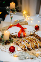 Traditional Christmas stollen made of dried fruits and nuts sprinkled with powdered sugar on the background of a Christmas decor with candles. Traditional Christmas cupcake.