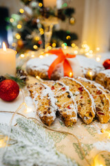 Fototapeta na wymiar Traditional Christmas stollen made of dried fruits and nuts sprinkled with powdered sugar on the background of a Christmas decor with candles. Traditional Christmas cupcake.