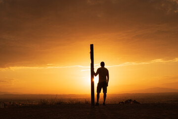 Orange sunset with a silhouette of a man leaning on a log looking to the horizon thinking about the future