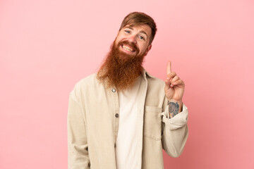 Young reddish caucasian man isolated on pink background showing and lifting a finger in sign of the best