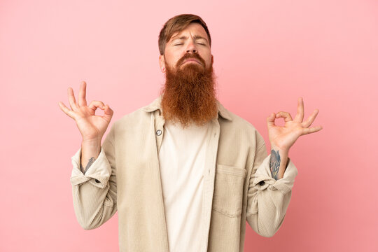 Young reddish caucasian man isolated on pink background in zen pose