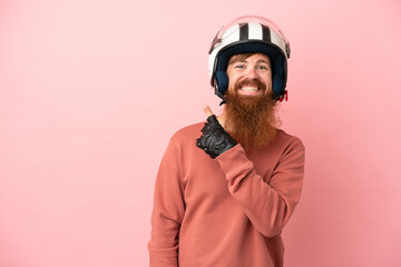 Young reddish caucasian man with a motorcycle helmet isolated on pink background pointing to the side to present a product