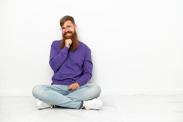 Young caucasian reddish man sitting on the floor isolated on white background with glasses and smiling
