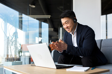 Asian call center employee talking to customers sitting in office, Asian businessman using headset and laptop for video call happy and smiling