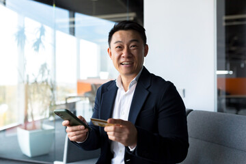 Happy asian man shopping online, businessman in office, shopping in online store using credit card, happy with the loan