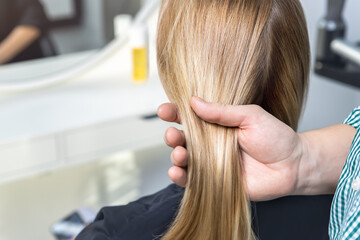 Close-up male professional hairdresser stylist hand hold woman long strong smooth shining dyed golden hair lock. Female person client back new hairstyle look at beaty salon. Hair care and treatment