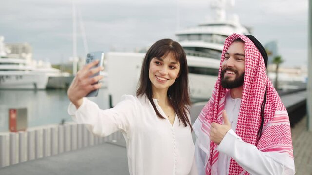 Young european businesswoman taking selfie with happy arab man client after successful deal in port