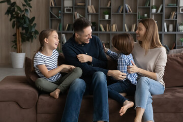 Happy two generations family tickling, playing on cozy sofa at home. Joyful little kids boy girl...