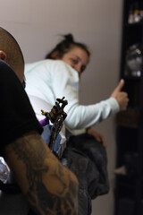 Woman gesturing being okay while is tattooed by a tatoo artist in studio