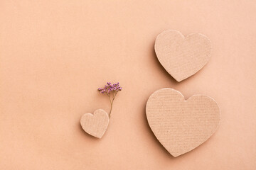 Fototapeta premium Family concept. Three cardboard hearts - dad, mom and baby with a dry flower on a beige background. Top and vertical view.