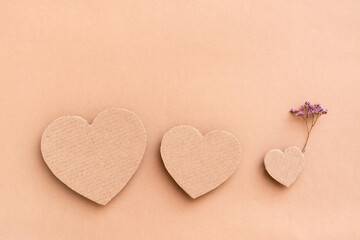 Family concept. Three cardboard hearts - parents and a child with a flower on a beige background. Top view. Copy space