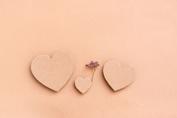 Obraz premium Family concept. Three cardboard hearts - a child with a dry flower between parents on a beige background. Top view.
