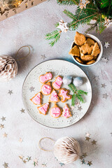 Freshly baked Christmas cookies with pink icing on a plate on a decorated table. Festive treat. Top and vertical view. Close-up