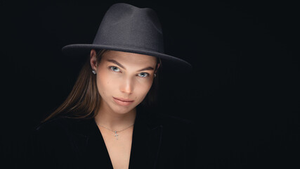 Fashionable studio portrait of a beautiful young girl in black hat on a black background. Low key.