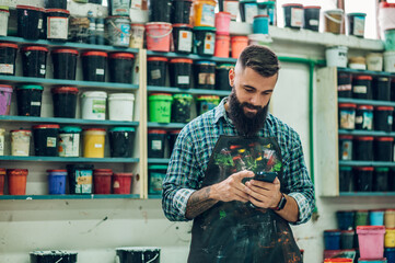 Male worker mixing colors for screen printing in a workshop and using a smartphone