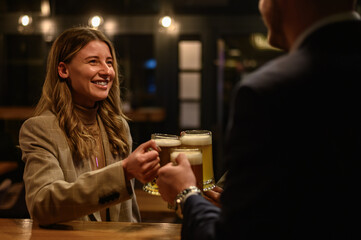 Cheerful colleagues drinking beer in the bar together after work and using a tablet