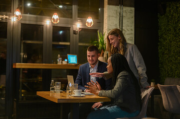 Cheerful work colleagues working on a laptop while having a meeting in a cafe