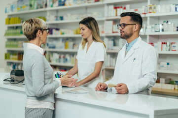 Fototapeta na wymiar Two pharmacist giving prescription medications to senior female customer in a pharmacy