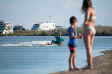 Fototapeta na wymiar Kitesurfer athlete surfing on sea surface in front of kids watching him