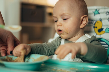 Adorable little baby eating his dinner and making a mess