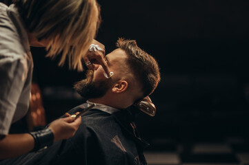 Fototapeta premium Man getting shaved with straight edge razor by hairdresser at barbershop