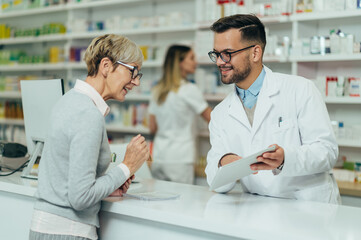 Young male pharmacist giving prescription medications to senior female customer in a pharmacy - obrazy, fototapety, plakaty