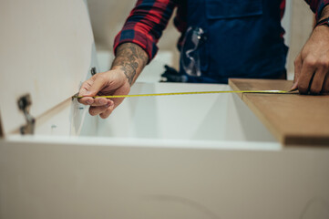 Young male carpenter working in workshop and measuring with meter