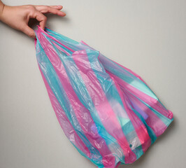 female hand holds full plastic bag on gray background, top view