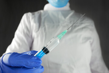 A nurse's hand in a blue medical glove with a disposable syringe, close-up,  gray background. A nurse holds a syringe before vaccination.