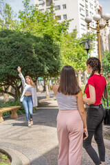 Three friends meeting in a square. Two women greet the newcomer. With one arm raised.