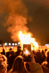 Fototapeta na wymiar Young female recording a video with her phone of a bonfire during the new year's eve festivities